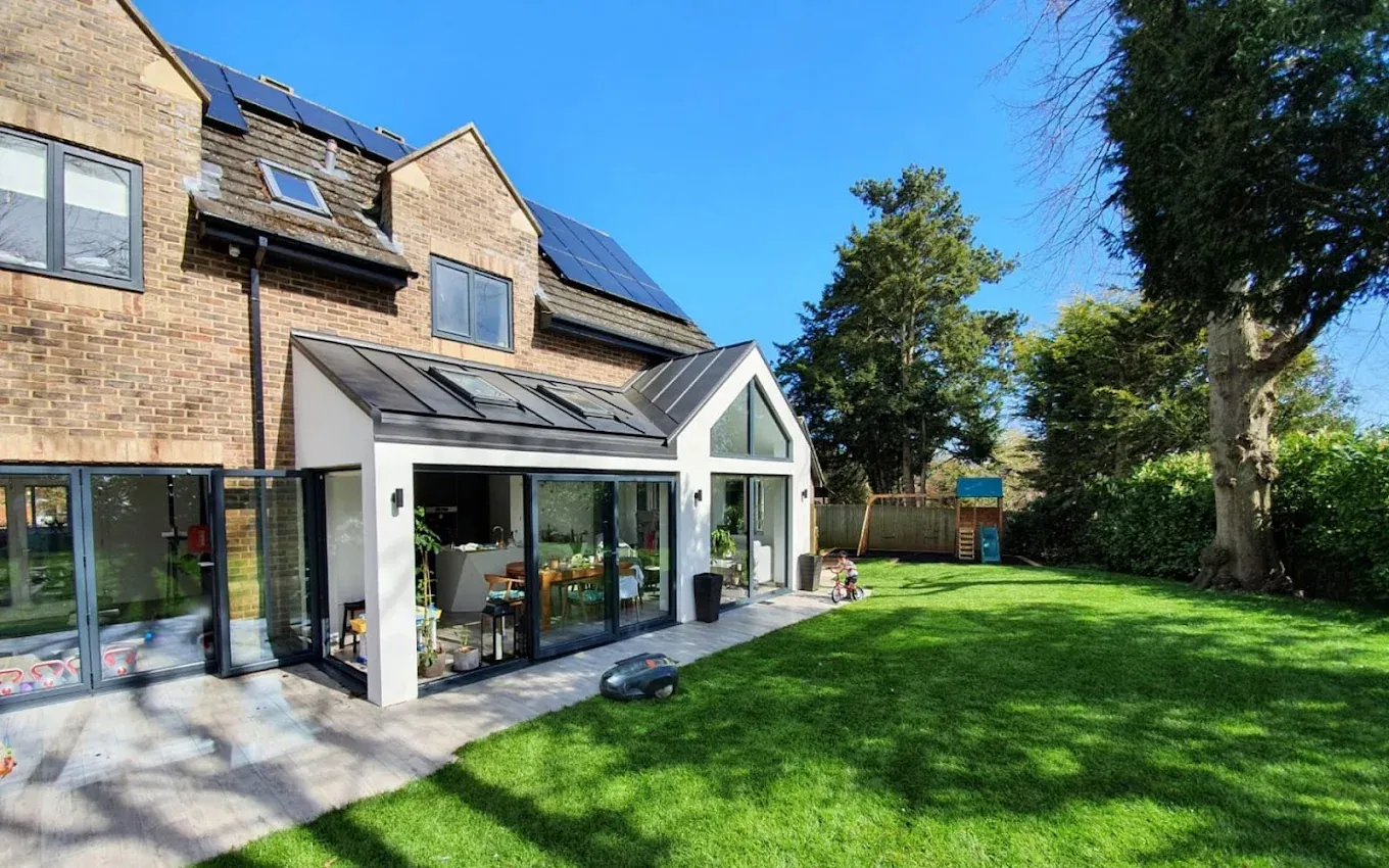 A glazed orangery extension with a pitched glass roof and bifold doors, opening onto a lawn with a mature tree A glazed orangery extension with a pitched glass roof and bifold doors, opening onto a lawn with a mature tree