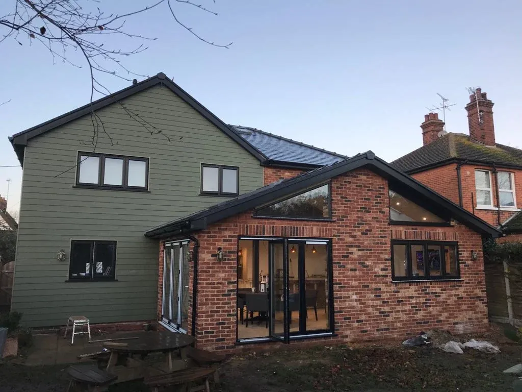 A green-clad house with a brick extension and bifold doors, photographed at dusk A green-clad house with a brick extension and bifold doors, photographed at dusk