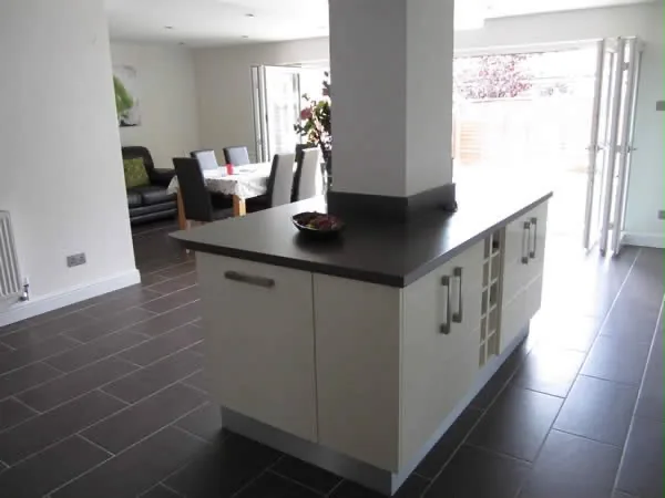 A finished kitchen island with a dark worktop, dining table and bifold doors beyond