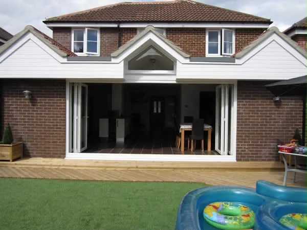 The finished rear elevation with twin gables and the bifold doors folded fully open onto decking The finished rear elevation with twin gables and the bifold doors folded fully open onto decking