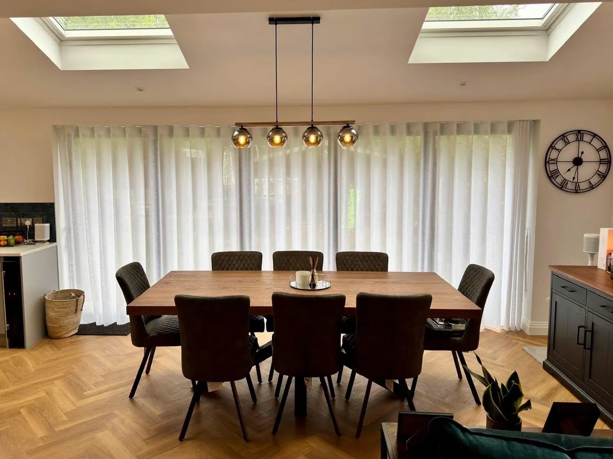 A dining table beneath two rooflights with full-width sheer curtains behind