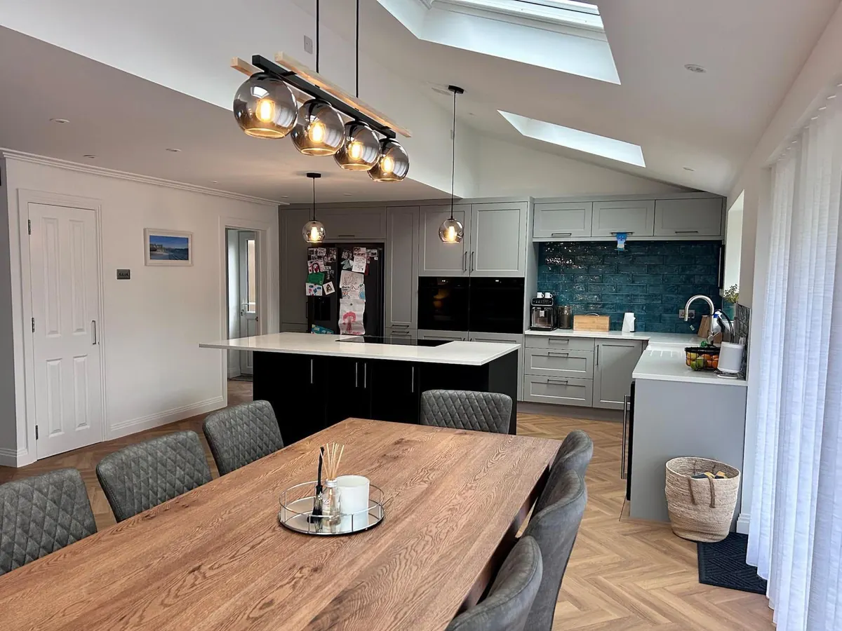 An open-plan kitchen and dining room with grey shaker units, a dark island and rooflights above
