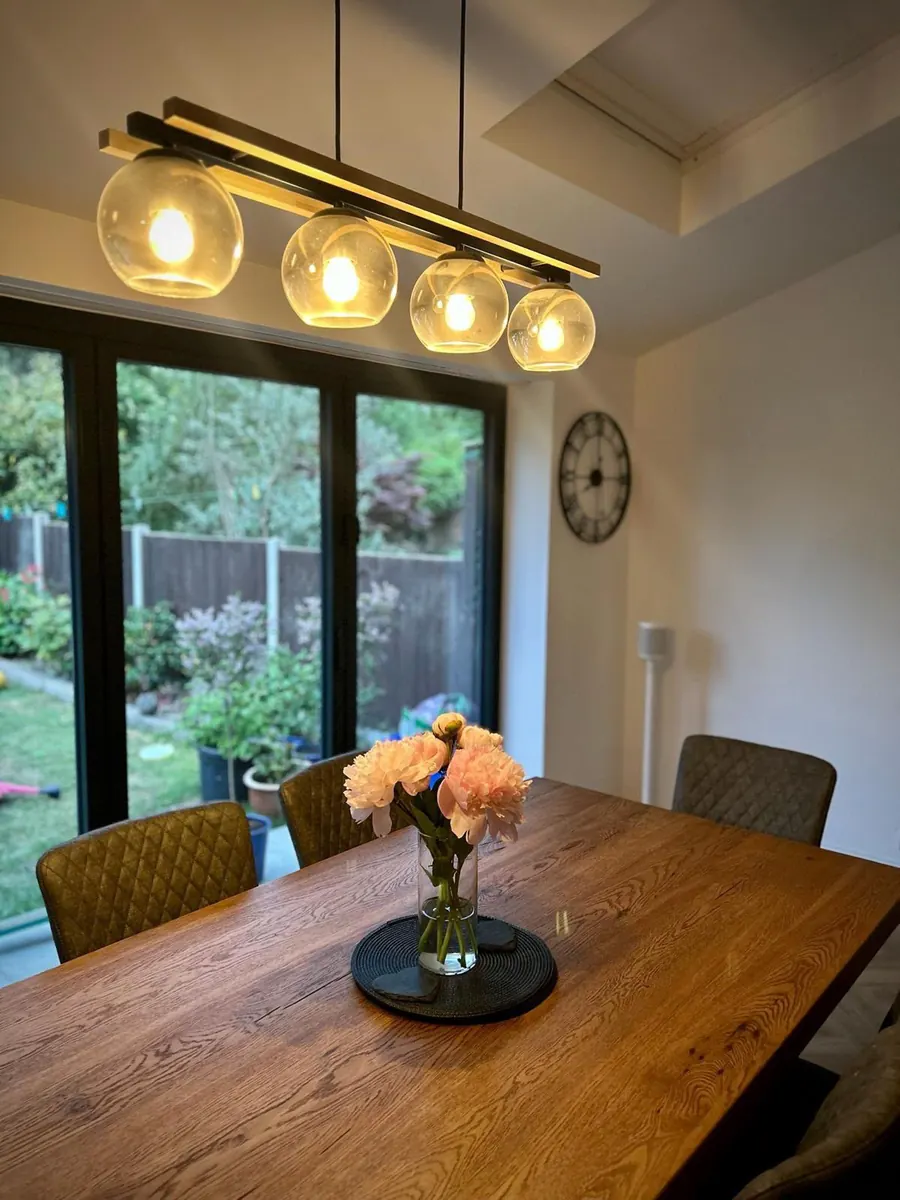 A pendant light with four glass globes above an oak dining table, garden doors beyond