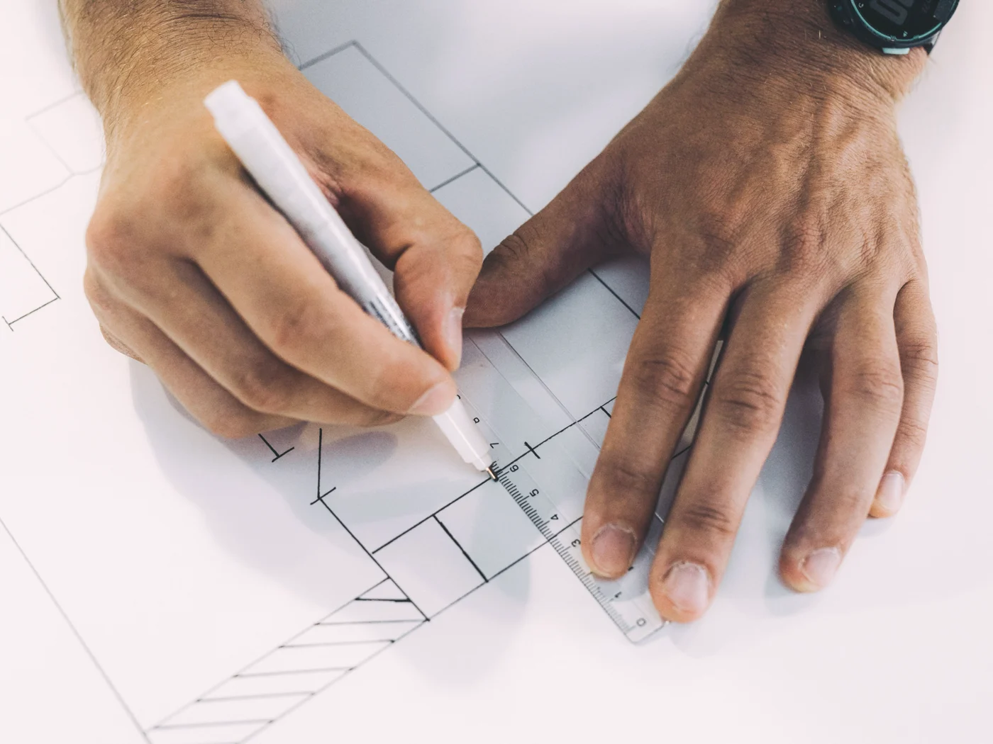 Hands drawing a floor plan with a pen and scale rule