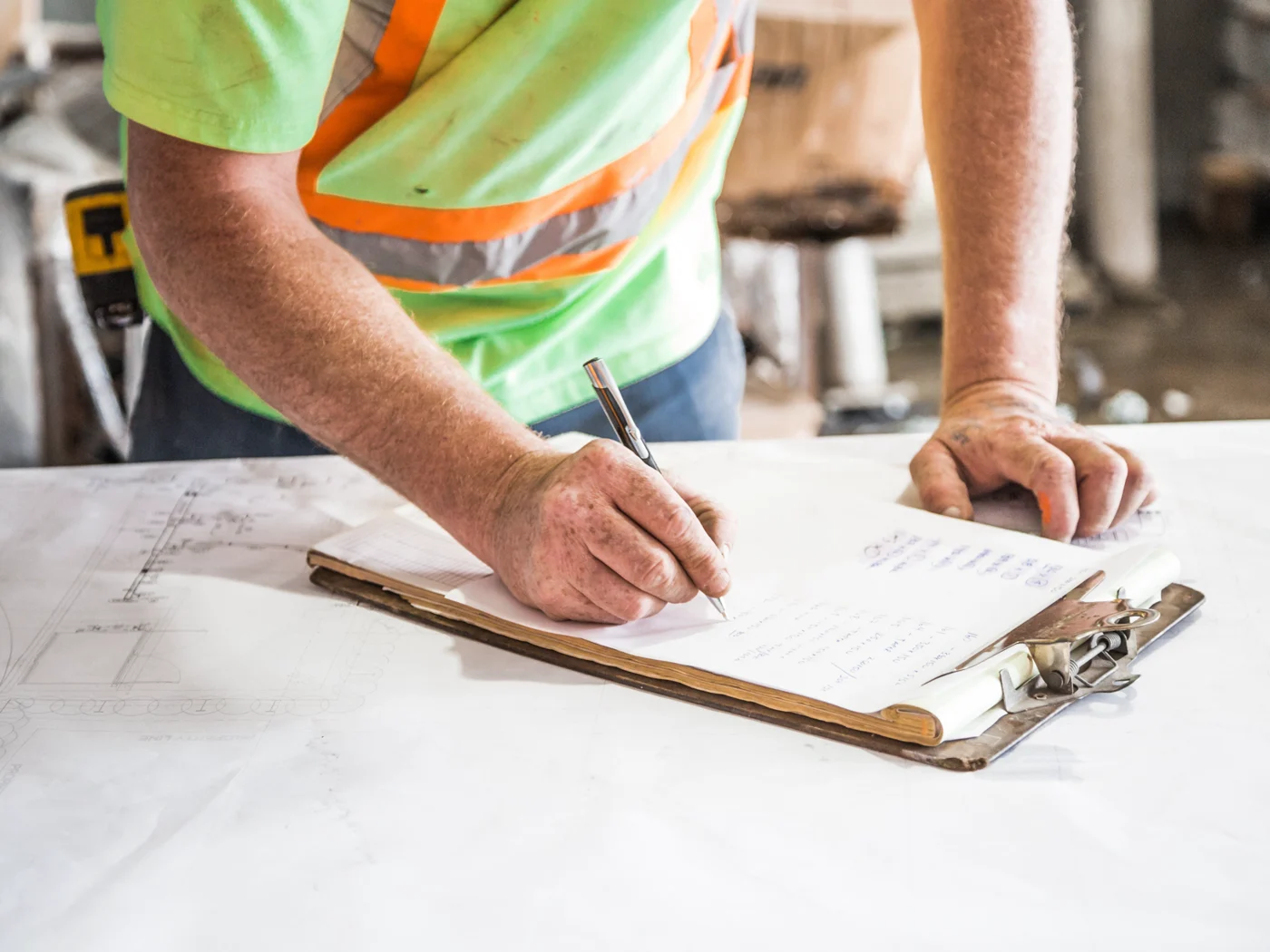 A site manager writing up notes on a clipboard over a set of drawings